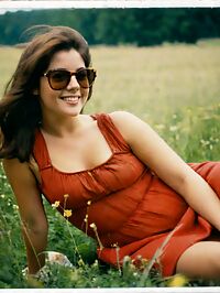 A 21 year old woman with short hair and a red dress lounges in a sunlit meadow